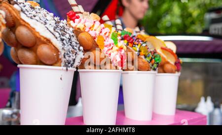 Bubble Waffeln mit Himbeeren, Schokolade und Marshmallows in white paper Cups sind auf offene Küche Food Festival verkauft. Hong Kong Waffeln. Anhand von quantitativen Simulatio Stockfoto