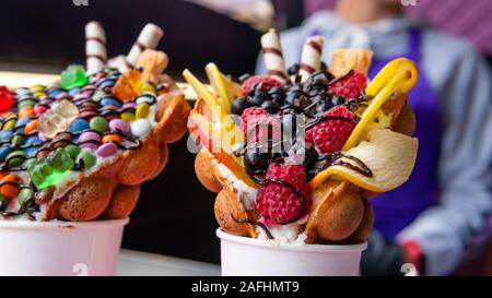 Bubble Waffeln mit Himbeeren, Schokolade und Marshmallows in white paper Cups sind auf offene Küche Food Festival verkauft. Hong Kong Waffeln. Anhand von quantitativen Simulatio Stockfoto