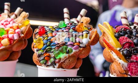 Bubble Waffeln mit Himbeeren, Schokolade und Marshmallows in white paper Cups sind auf offene Küche Food Festival verkauft. Hong Kong Waffeln. Anhand von quantitativen Simulatio Stockfoto