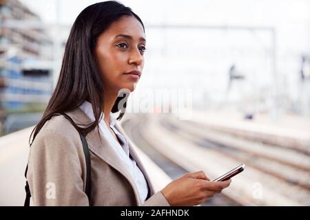 Geschäftsfrau auf Bahnsteig Pendeln zur Arbeit Buchung Ticket auf dem Mobiltelefon Stockfoto