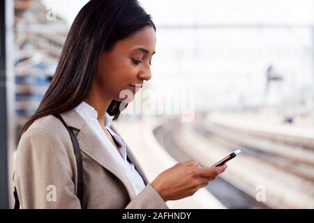 Geschäftsfrau auf Bahnsteig Pendeln zur Arbeit Buchung Ticket auf dem Mobiltelefon Stockfoto
