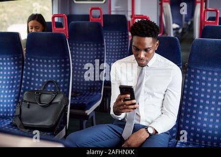 Geschäftsmann sitzt in dem Zug Pendeln zum Arbeitsplatz Abrufen von Nachrichten auf dem Handy Stockfoto