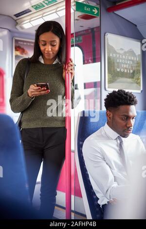 Weibliche Passagier durch Türen in Zug am Handy suchen Stehend Stockfoto