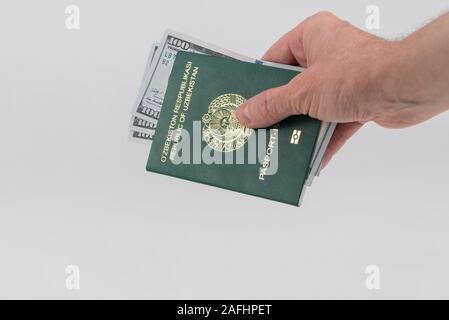 Hand hält aus Usbekistan Reisepass mit USA Dollar. Konzept - Bestechendem und Korruption Stockfoto