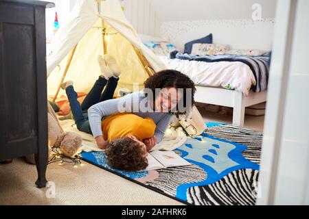 Einzelne Mutter kitzeln Sohn als Sie lesen In der Höhle im Schlafzimmer zu Hause Stockfoto