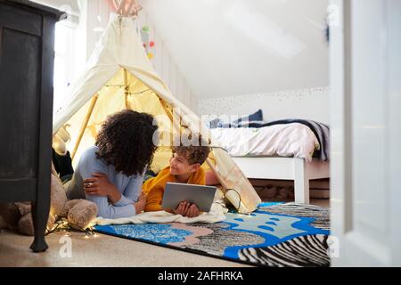 Single Mutter spielt mit Sohn auf Digital Tablet in der Höhle im Schlafzimmer zu Hause Stockfoto