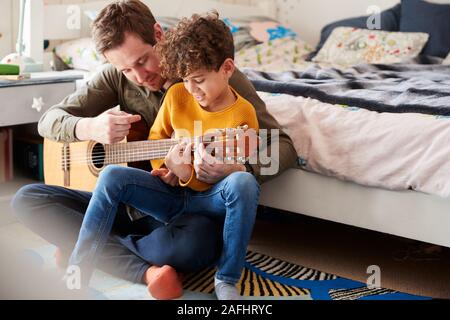 Einzelnen Vater zu Hause mit Sohn lehrte ihn zu spielen akustische Gitarre im Schlafzimmer Stockfoto