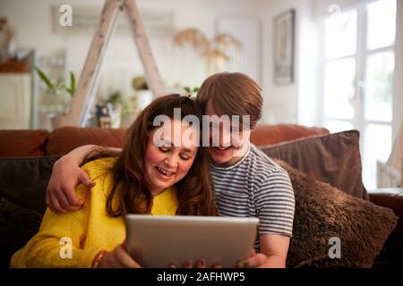 Liebevolle Junge Abstiegsyndrom Paar sitzt auf einem Sofa mit digitalen Tablette zu Hause Stockfoto