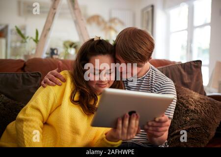 Liebevolle Junge Abstiegsyndrom Paar sitzt auf einem Sofa mit digitalen Tablette zu Hause Stockfoto