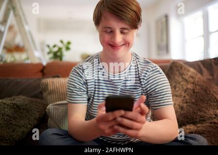 Junge Abstiegsyndrom Mann sitzt auf einem Sofa mit Handy zu Hause Stockfoto