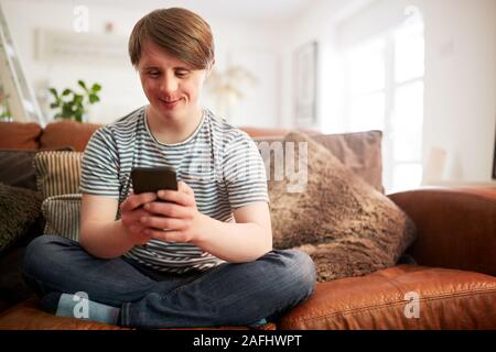 Junge Abstiegsyndrom Mann sitzt auf einem Sofa mit Handy zu Hause Stockfoto