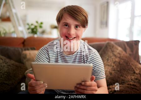 Porträt der jungen Abstiegsyndrom Mann sitzt auf einem Sofa mit digitalen Tablette zu Hause Stockfoto