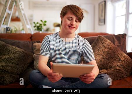 Junge Abstiegsyndrom Mann sitzt auf einem Sofa mit digitalen Tablette zu Hause Stockfoto