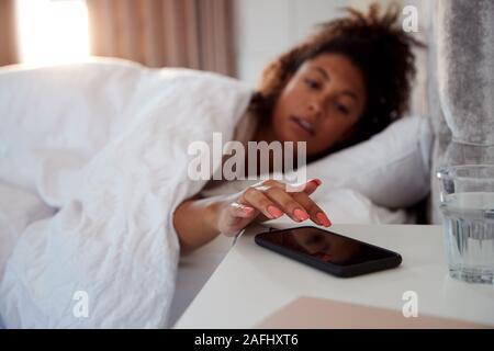 Frau Aufwachen im Bett erreicht Die Schalten Sie Alarm am Handy Stockfoto