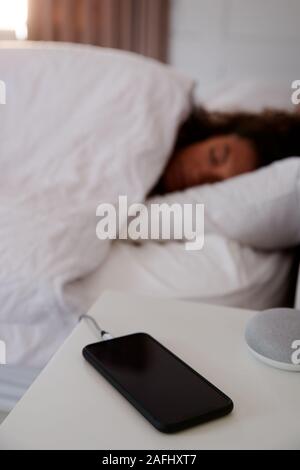Frau schläft im Bett mit Handy auf Nachttisch Stockfoto