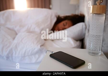 Frau schläft im Bett mit Handy auf Nachttisch Stockfoto