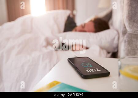 Mann der schläft im Bett mit Handy auf dem Nachttisch Stockfoto