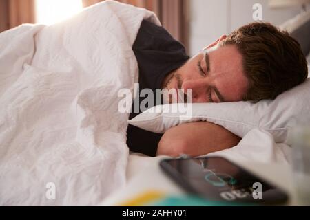 Mann der schläft im Bett mit Handy auf dem Nachttisch Stockfoto