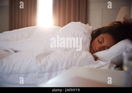 Friedliche Frau schlafend im Bett als Tag Pause durch Vorhänge Stockfoto