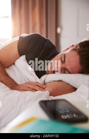 Mann der schläft im Bett mit Handy auf dem Nachttisch Stockfoto