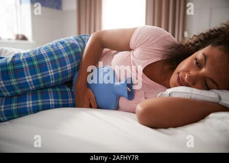 Frau mit Schlafanzug Leiden mit der Zeit Schmerzen im Bett liegend mit Wärmflasche Stockfoto