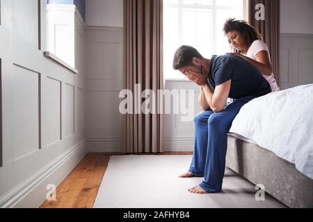 Frau tröstend Mann mit Schlafanzug mit Depression sitzen auf dem Bett zu Hause Leiden Stockfoto