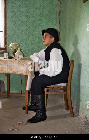 Ivanovo, Serbien, 15. April 2018. Ein einsamer Junge mit Hut ist allein sitzen an einem Tisch in einem Zimmer und denkt über sein Leben. Die Zimmer auch Wi Stockfoto