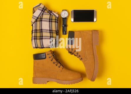 Layout der Herbst Kleidung und Accessoires in warmen Farben auf einem gelben Hintergrund. Jeans, Hemd, Schuhe, Telefon und schauen Sie sich flach in der Nähe. Stockfoto