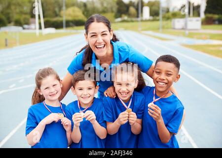 Portrait von Kindern mit weiblichen Trainer zeigen, ein Sieger Medaillen auf Sport Tag