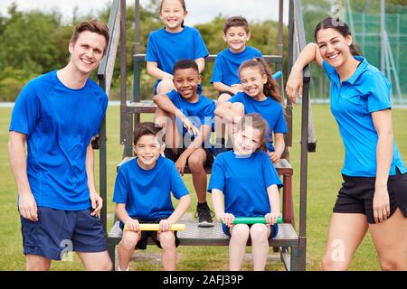 Portrait von Kindern mit männlichen und weiblichen Trainer Vorbereitung für Relais Rennen am Tag des Sports Stockfoto