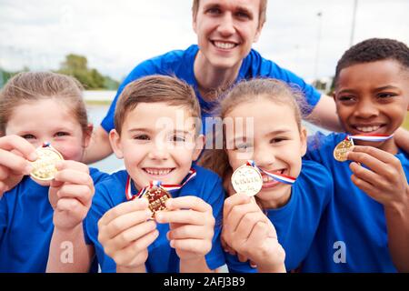 Portrait von Kindern mit männlichen Trainer zeigen, ein Sieger Medaillen auf Sport Tag