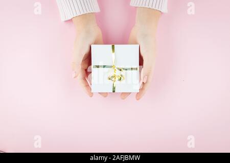 Flach von Mädchen Hände halten Geschenk verpackt und mit Bogen auf rosa Hintergrund mit Kopie Raum eingerichtet. Weihnachten, Geburtstag und Urlaub Konzept, Kopieren Stockfoto