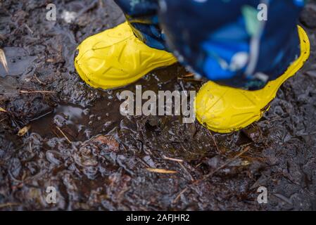 Ein kleines Kind in gelben Gummistiefeln steht im Schlamm Stockfoto