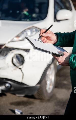 Insurance Agent prüft und den Schaden am Auto zu untersuchen nach einem Unfall. Inspektion des Autos nach einem Unfall auf der Straße. Die vordere fende Stockfoto