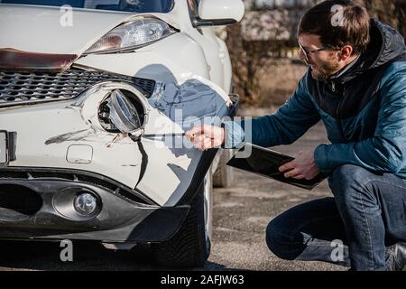 Insurance Agent prüft und den Schaden am Auto zu untersuchen nach einem Unfall. Inspektion des Autos nach einem Unfall auf der Straße. Die vordere fende Stockfoto