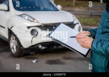 Insurance Agent prüft und den Schaden am Auto zu untersuchen nach einem Unfall. Inspektion des Autos nach einem Unfall auf der Straße. Die vordere fende Stockfoto