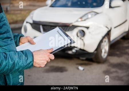 Insurance Agent prüft und den Schaden am Auto zu untersuchen nach einem Unfall. Inspektion des Autos nach einem Unfall auf der Straße. Die vordere fende Stockfoto