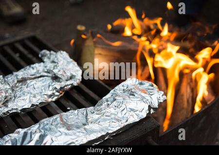 Köstliche Mahlzeit eingewickelt in Alufolie kochen über Feuer auf dem Campingplatz Stockfoto