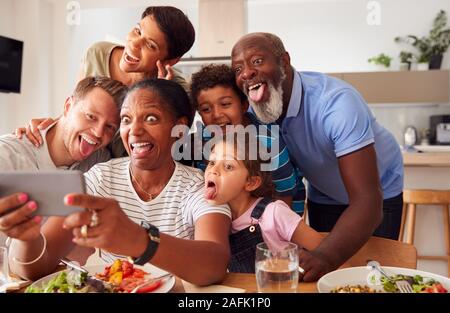 Multi-Generation gemischten Rennen Familie Posieren für selfie wie Sie Essen, Essen um den Tisch zu Hause zusammen Stockfoto