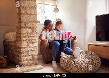 Großmutter saß im Stuhl mit Enkelin aufzupassen Film auf Digital Tablet zusammen Stockfoto