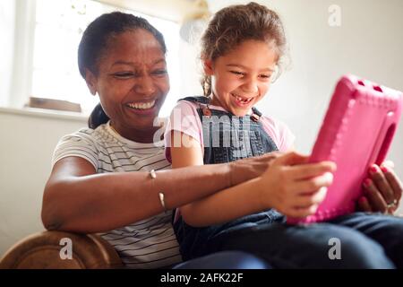 Großmutter saß im Stuhl mit Enkelin aufzupassen Film auf Digital Tablet zusammen Stockfoto
