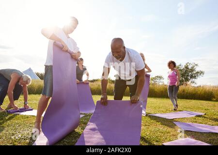 Gruppe von Reife Männer und Frauen Einrollen Trainingsmatten am Ende der Outdoor Yoga Klasse Stockfoto