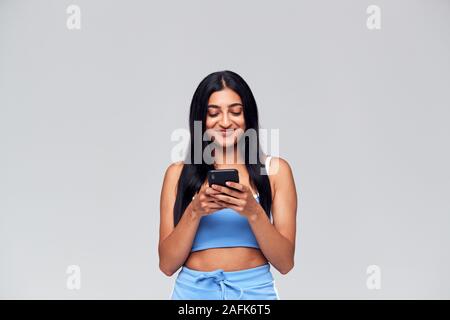 Studio Geschossen von Kausal gekleidete junge Frau mit Handy aus Kamera suchen Stockfoto