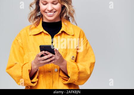 Studio Shot von lächelnden Kausal gekleidete junge Frau mit Mobiltelefon Stockfoto
