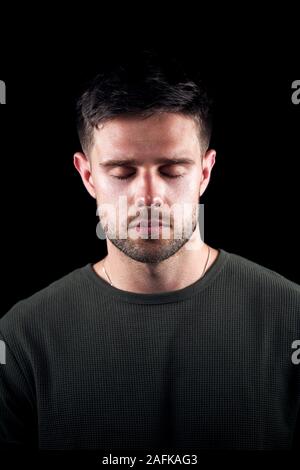 Studio Portrait des jungen Mannes mit ernsten Ausdruck und geschlossenen Augen auf schwarzem Hintergrund Stockfoto