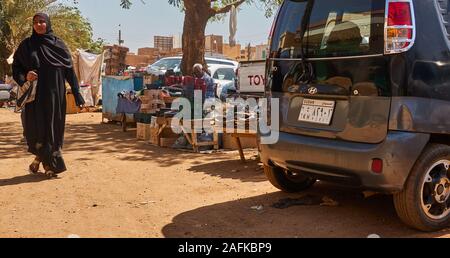 Khartum, Sudan, Ca. Februar 8., 2019: Markt in Khartum ausgeht, mit einem kleinen Auto und eine Frau in der traditionellen schwarzen Kleidung Stockfoto