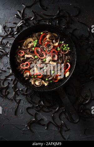 Gesunde vegetarische Nahrung. Vollkorn glutenfreie Roggen Malz Pasta mit Pilzen und Gemüse in gusseisernen Pfanne auf schwarzem Hintergrund oben Ansichtskopie Raum Stockfoto