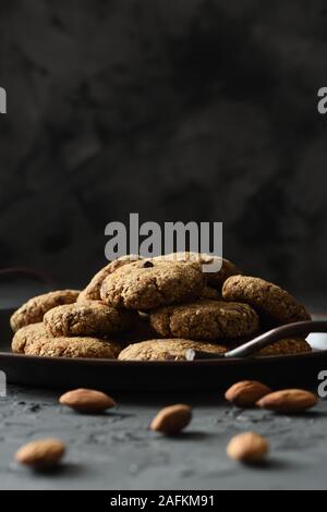 Glutenfrei vegan Süßigkeiten Konzept. Almond cookies mit Schokolade Tropfen in vintage Fach und ganze Mandel Muttern auf schwarzem Hintergrund Seitenansicht Kopie Raum l Stockfoto