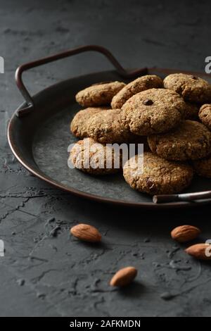 Glutenfrei vegan cookies Konzept. Mandelplätzchen in vintage Fach und ganze Mandel Muttern auf schwarzem Hintergrund Seitenansicht kopieren Platz Low Key still life Stockfoto