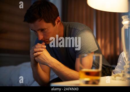 Deprimiert Mann mit Schlafanzug saß an der Seite des Bett mit Glas Whisky am Nachttisch Stockfoto
